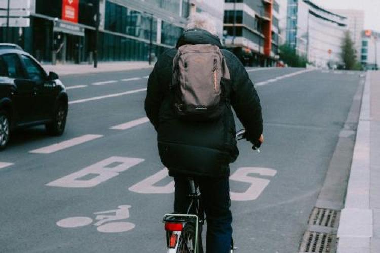 Een fietser met een regenjas en een rugzak aan is op weg naar zijn werk. 